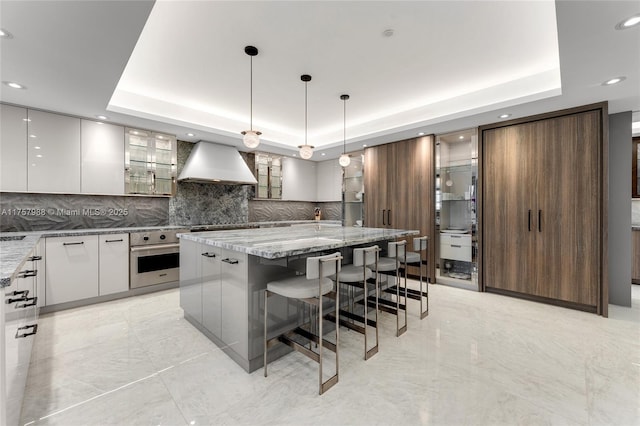 kitchen featuring a tray ceiling, oven, and wall chimney range hood