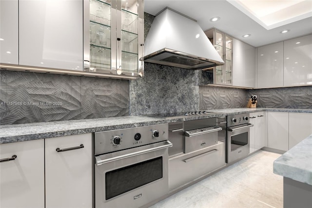 kitchen featuring modern cabinets, backsplash, stainless steel oven, and island range hood