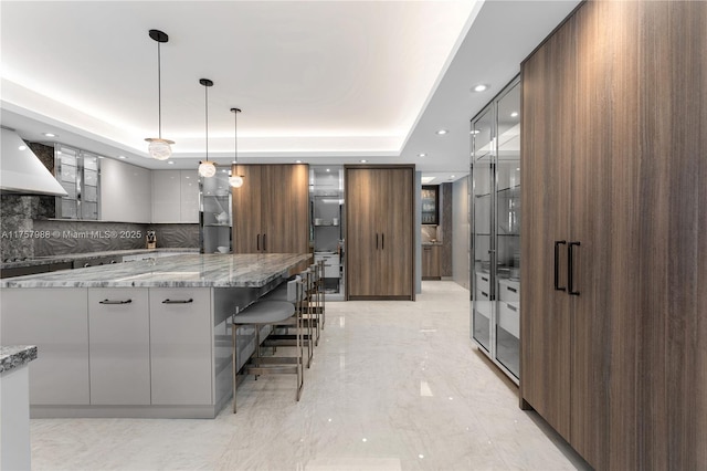 kitchen with stone counters, a raised ceiling, modern cabinets, a kitchen bar, and glass insert cabinets