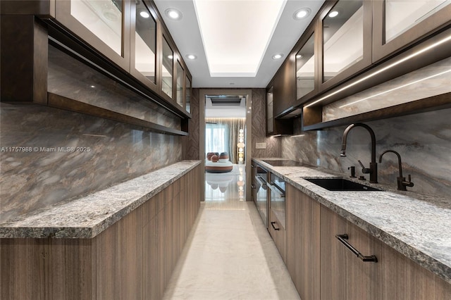 kitchen featuring light stone counters, backsplash, glass insert cabinets, a sink, and modern cabinets