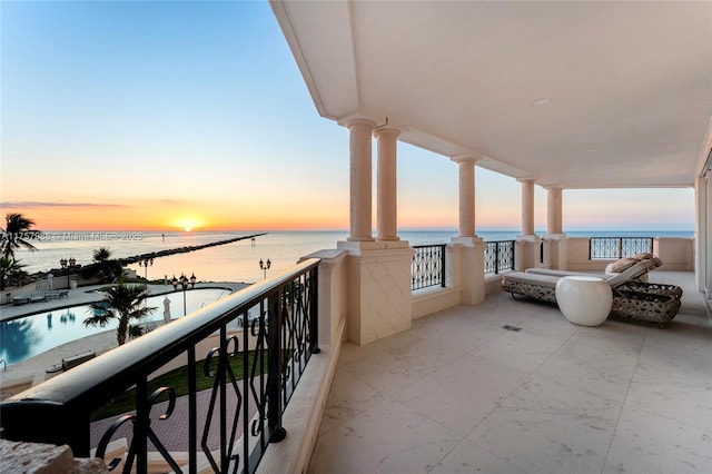 balcony at dusk featuring a water view