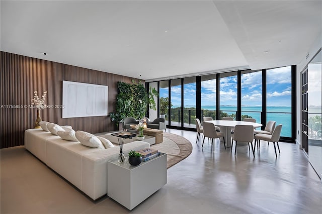 living room with wood walls, a water view, finished concrete floors, and floor to ceiling windows