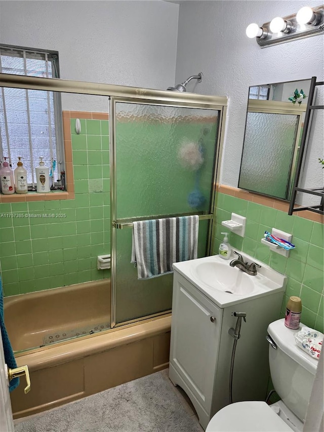 bathroom featuring wainscoting, toilet, enclosed tub / shower combo, vanity, and tile walls