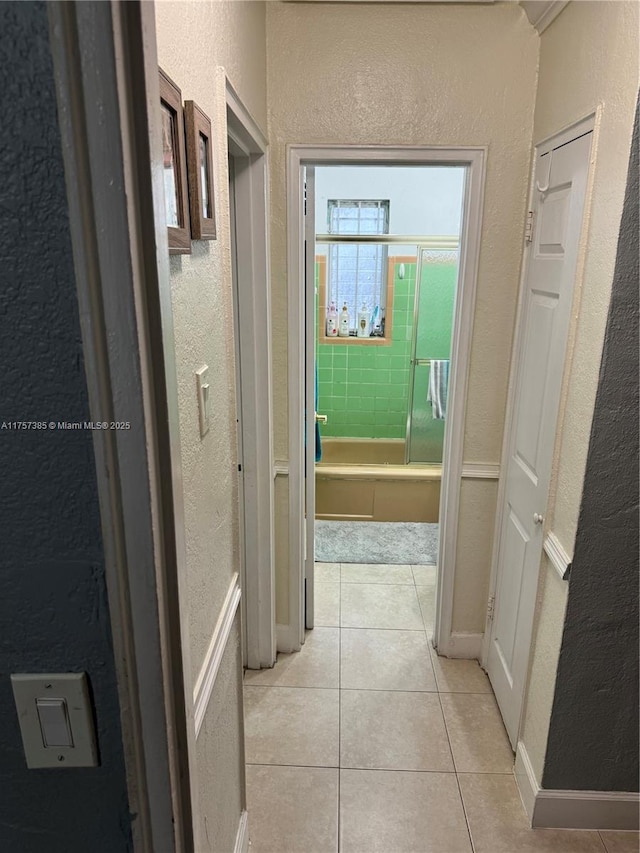 hall featuring a textured wall and light tile patterned floors