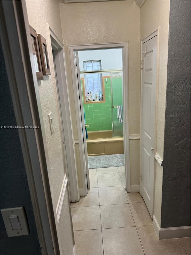 corridor with a textured wall, baseboards, and light tile patterned floors