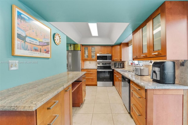 kitchen with stainless steel appliances, tasteful backsplash, brown cabinetry, and light tile patterned flooring