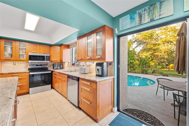 kitchen featuring light tile patterned floors, stainless steel appliances, backsplash, and glass insert cabinets