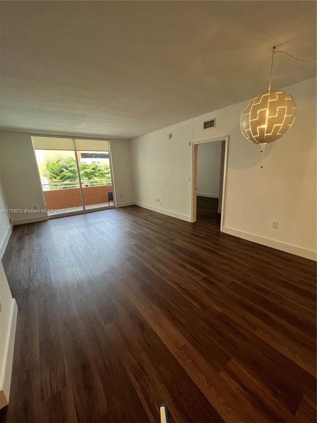 unfurnished living room featuring a notable chandelier, visible vents, baseboards, and dark wood-style flooring