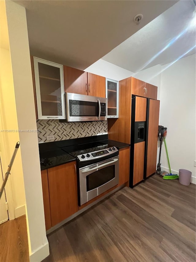 kitchen featuring dark wood-type flooring, appliances with stainless steel finishes, brown cabinets, dark countertops, and glass insert cabinets