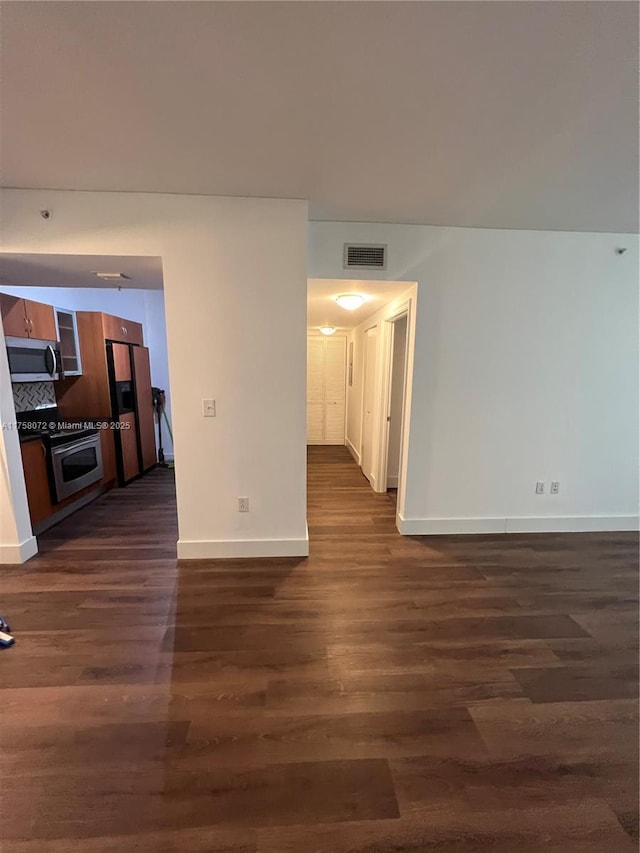 empty room featuring dark wood-type flooring, visible vents, and baseboards