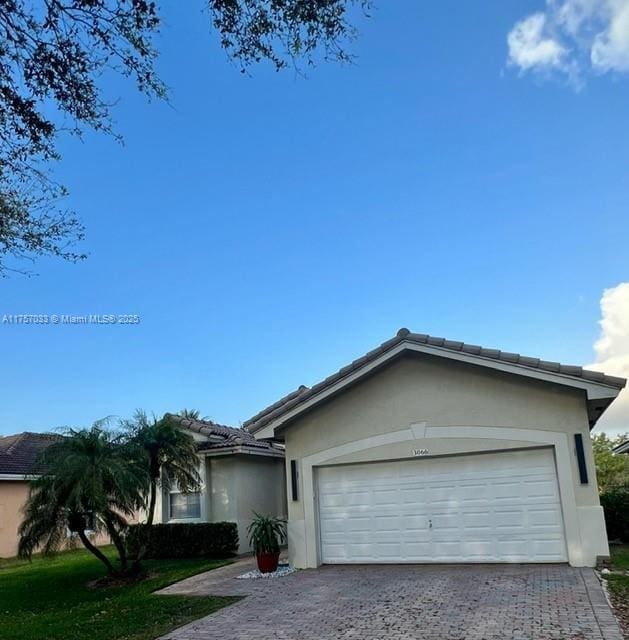 ranch-style home featuring a garage, a front lawn, decorative driveway, and stucco siding