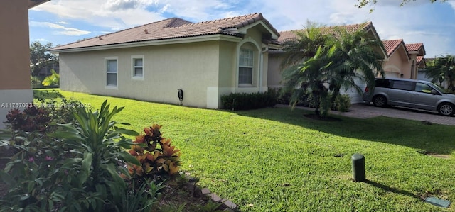 view of side of home with an attached garage, a tiled roof, a lawn, and stucco siding