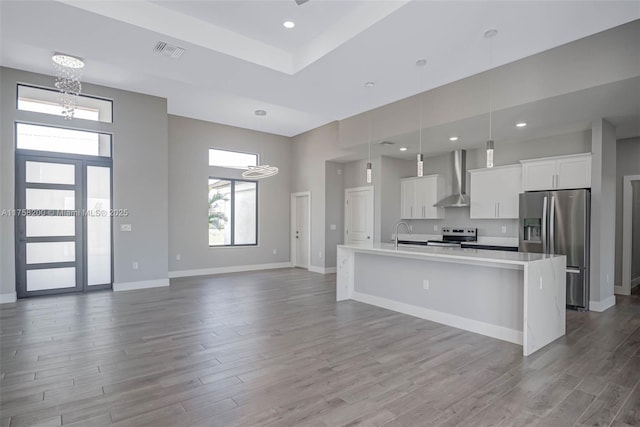 kitchen with an island with sink, appliances with stainless steel finishes, wood finished floors, wall chimney range hood, and white cabinetry