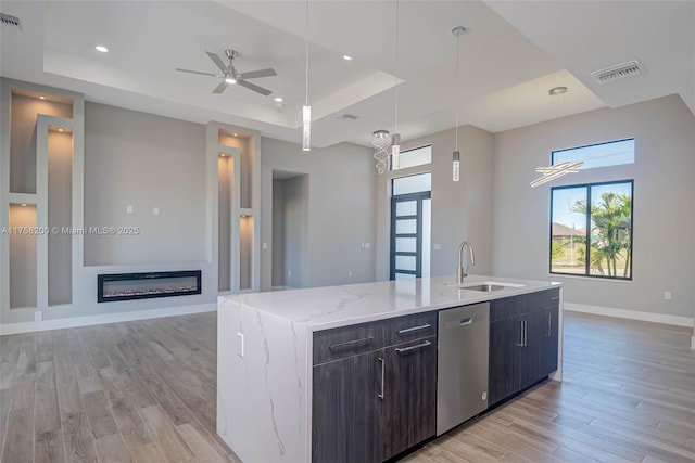 kitchen with a sink, a raised ceiling, dishwasher, and a glass covered fireplace