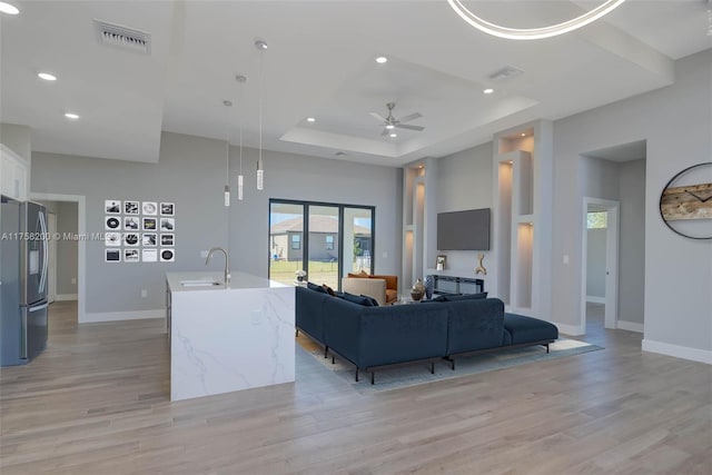 living room with visible vents, baseboards, a tray ceiling, light wood-type flooring, and recessed lighting