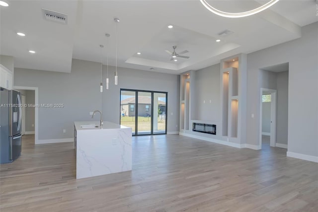 unfurnished living room with a raised ceiling, visible vents, a sink, and light wood finished floors