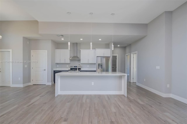 kitchen featuring stainless steel appliances, white cabinetry, light countertops, wall chimney exhaust hood, and a center island with sink