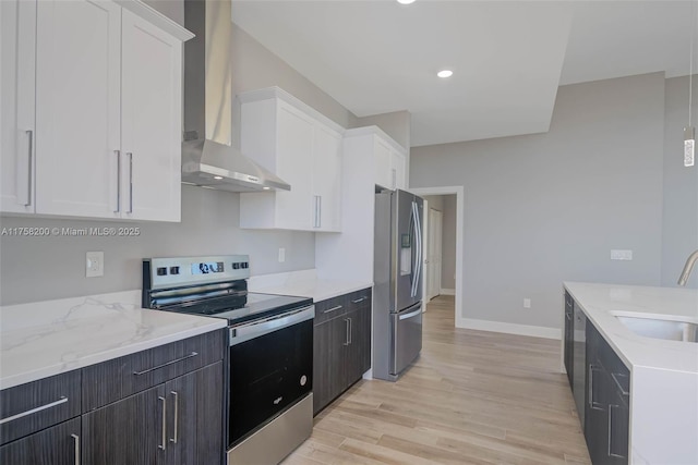 kitchen featuring light wood-style flooring, appliances with stainless steel finishes, white cabinets, a sink, and wall chimney exhaust hood