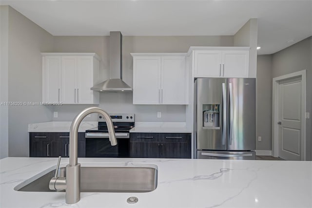 kitchen featuring light stone countertops, wall chimney exhaust hood, appliances with stainless steel finishes, and white cabinets