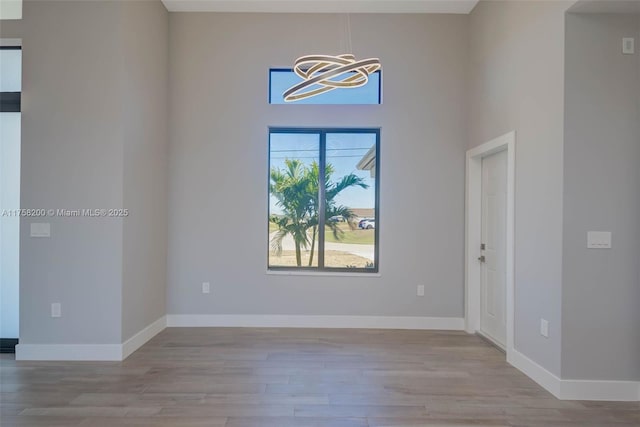 empty room with a notable chandelier, baseboards, and wood finished floors