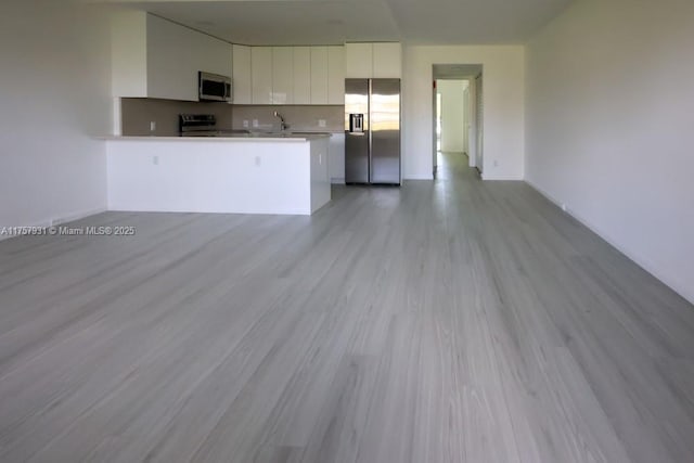 kitchen with appliances with stainless steel finishes, white cabinets, light wood-style floors, and a peninsula