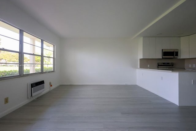 kitchen featuring a wall unit AC, light wood-style flooring, white cabinetry, light countertops, and stainless steel range with electric stovetop