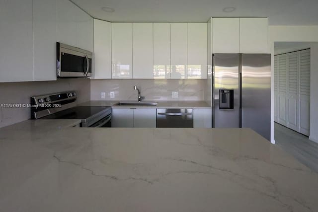 kitchen with stainless steel appliances, white cabinets, a sink, and light stone countertops