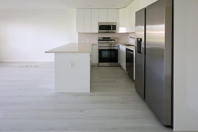 kitchen featuring light wood finished floors, stainless steel appliances, light countertops, white cabinetry, and a peninsula