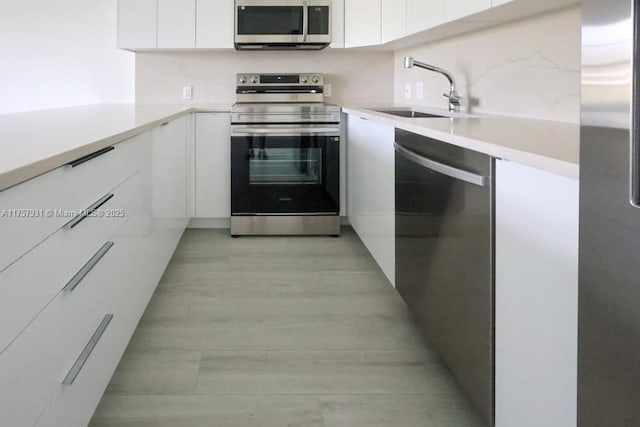 kitchen featuring stainless steel appliances, a sink, white cabinetry, light countertops, and modern cabinets