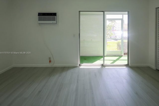 empty room featuring a wall unit AC, wood finished floors, and baseboards