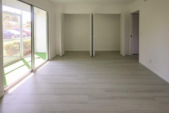 empty room with a healthy amount of sunlight, light wood-type flooring, and baseboards