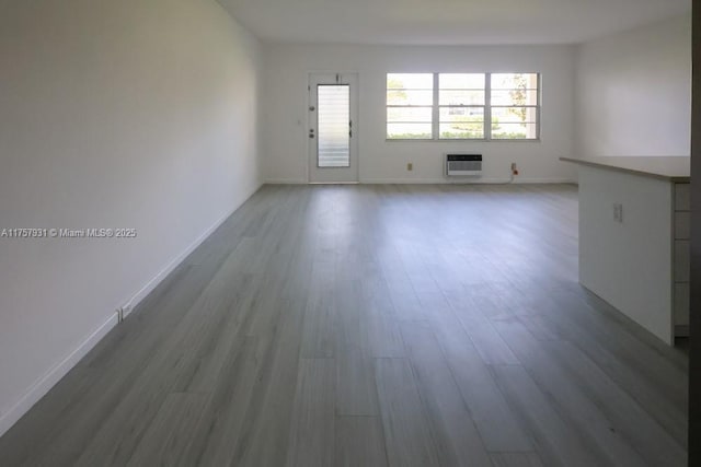 unfurnished living room with a wall mounted AC, baseboards, and wood finished floors