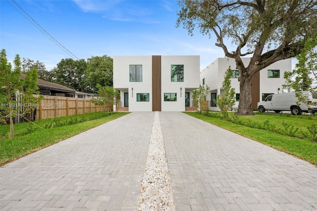 view of front of property with driveway, a front yard, fence, and stucco siding