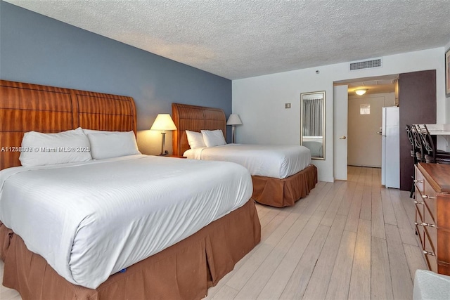 bedroom featuring freestanding refrigerator, visible vents, a textured ceiling, and light wood finished floors