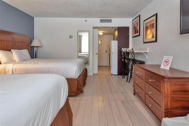 bedroom with light wood-style floors, freestanding refrigerator, visible vents, and a textured ceiling