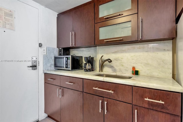 kitchen with light countertops, stainless steel microwave, a sink, and decorative backsplash