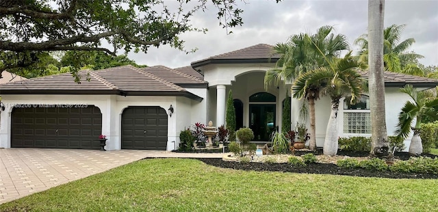 view of front of property featuring a tiled roof, a front yard, stucco siding, decorative driveway, and a garage