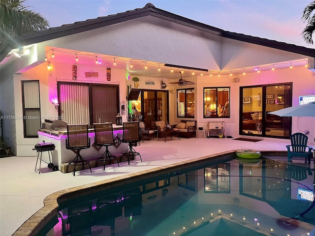 back of property at dusk featuring an outdoor pool, a patio area, and stucco siding