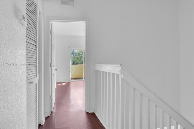 hallway featuring dark wood-style floors, visible vents, and an upstairs landing