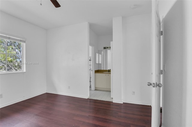 unfurnished bedroom featuring a sink, baseboards, wood finished floors, and ensuite bathroom