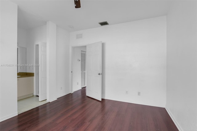 unfurnished bedroom with baseboards, visible vents, wood finished floors, and ensuite bathroom