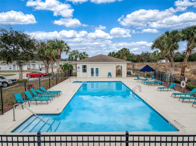 pool with a patio area, fence, and an outbuilding