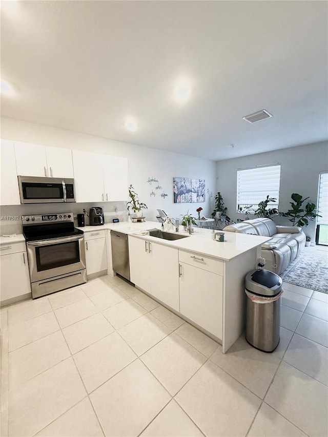 kitchen featuring light tile patterned floors, light countertops, appliances with stainless steel finishes, a sink, and a peninsula