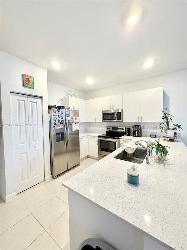 kitchen featuring stainless steel appliances, white cabinetry, a sink, light stone countertops, and a peninsula