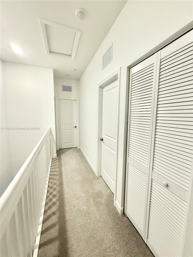 hallway with attic access, visible vents, light carpet, and baseboards