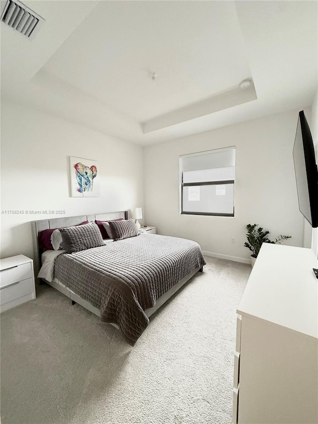 bedroom with light colored carpet, a raised ceiling, visible vents, and baseboards