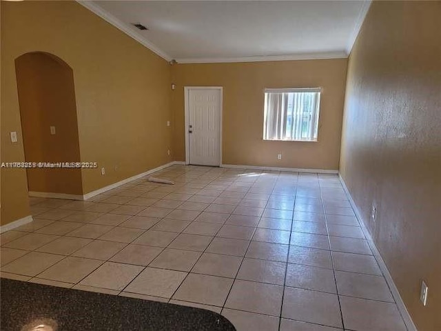 empty room with arched walkways, ornamental molding, light tile patterned floors, and baseboards