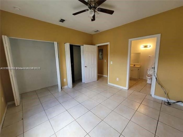 unfurnished bedroom with multiple closets, visible vents, light tile patterned flooring, ensuite bath, and baseboards