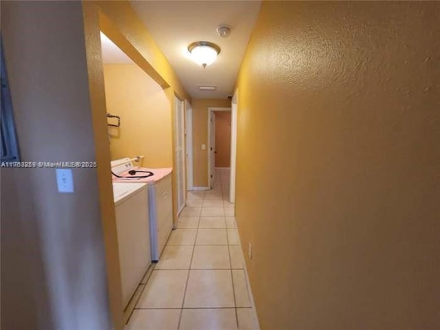 hall with independent washer and dryer and light tile patterned flooring