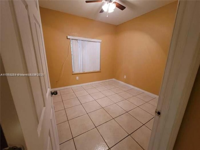 empty room featuring ceiling fan, light tile patterned flooring, and baseboards